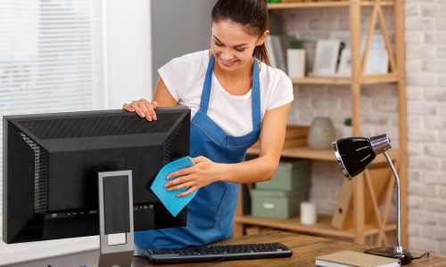 Studio shot of housekeeper. Beautiful woman cleaning computer at office and smiling